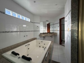 A modern bathroom with a large bathtub, a vanity with a mirror, and a shower area. - Joalpa Hotel Cabo Frio (Cabo Frio)