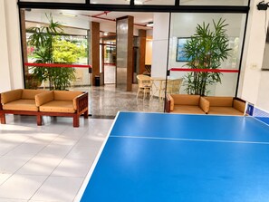 Une pièce avec une table de ping-pong, deux canapés et des plantes en pot.