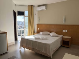 Habitación de hotel con cama, mesita de noche, aire acondicionado de pared y ventana con cortinas.