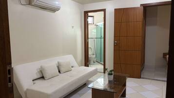 A room with a white sofa, a glass coffee table with a plant, and a wooden wardrobe.