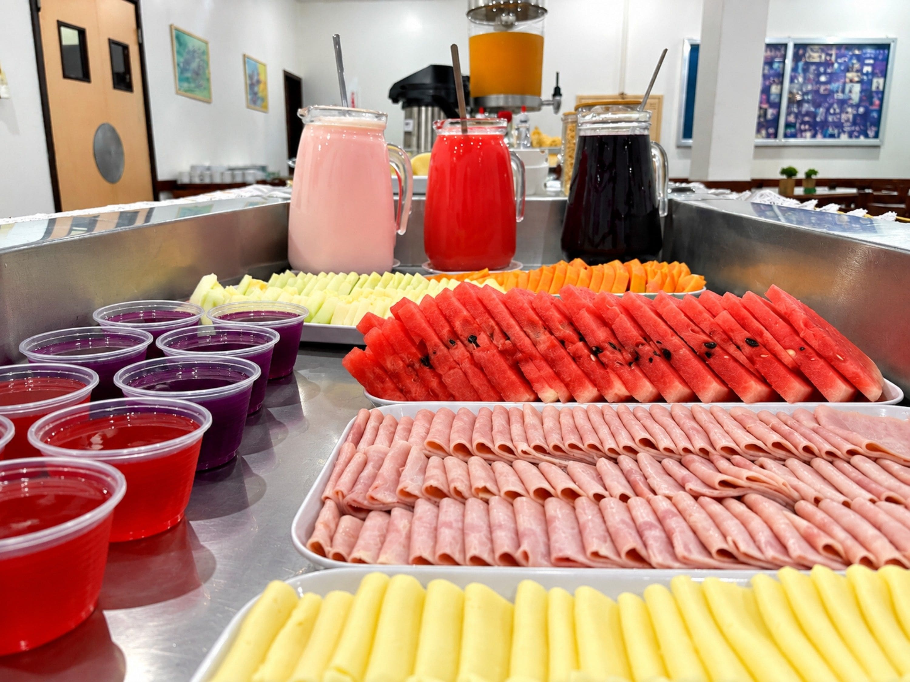 Ein Buffet mit verschiedenen Speisen, darunter Melone in Scheiben, Fleischröllchen und farbige Getränke.