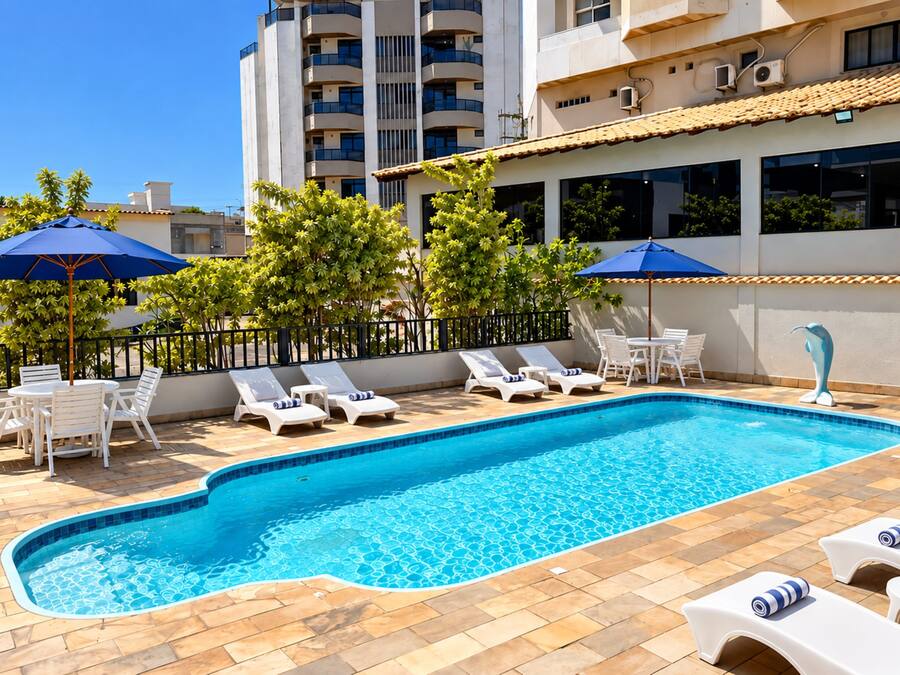Une piscine entourée de chaises longues et de parasols, bordée d’une terrasse carrelée et d’une petite clôture.