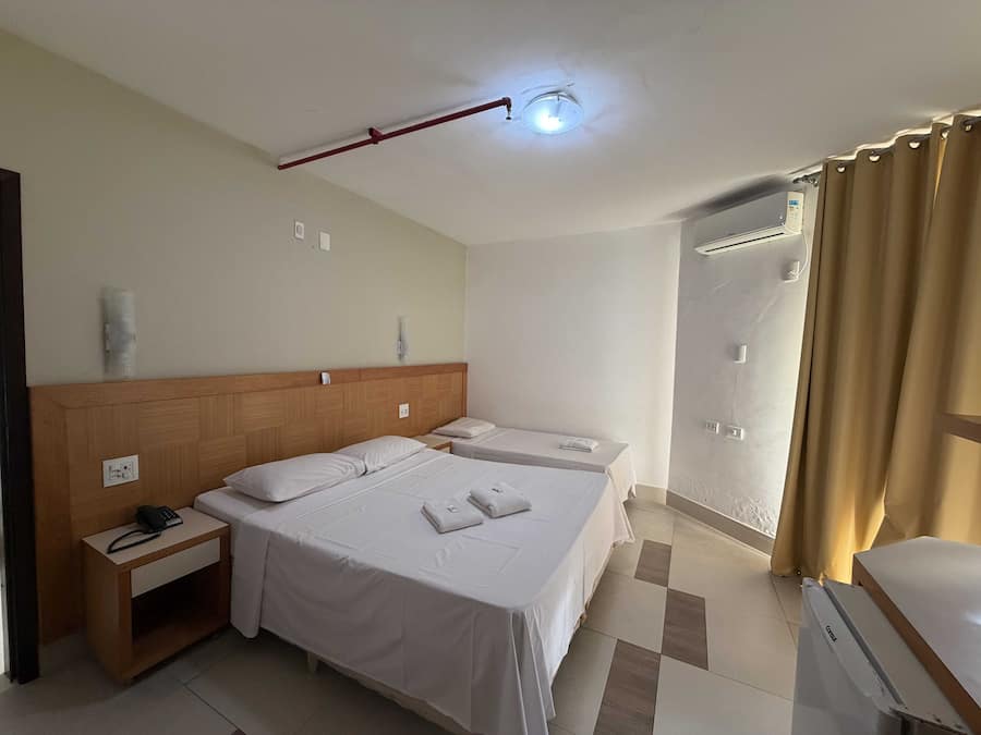 Habitación de hotel con una cama grande, mesitas de noche, teléfono y zona de ducha.