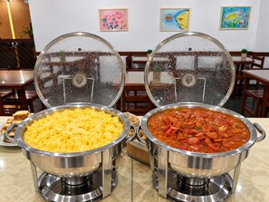 Deux plats de service en acier inoxydable, équipés de couvercles, dont l’un contient des œufs brouillés et l’autre un ragoût de légumes et de saucisses.