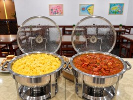 Dos platos chafing de acero inoxidable con tapas, uno con huevos revueltos y otro con guiso de verduras y salchicha.