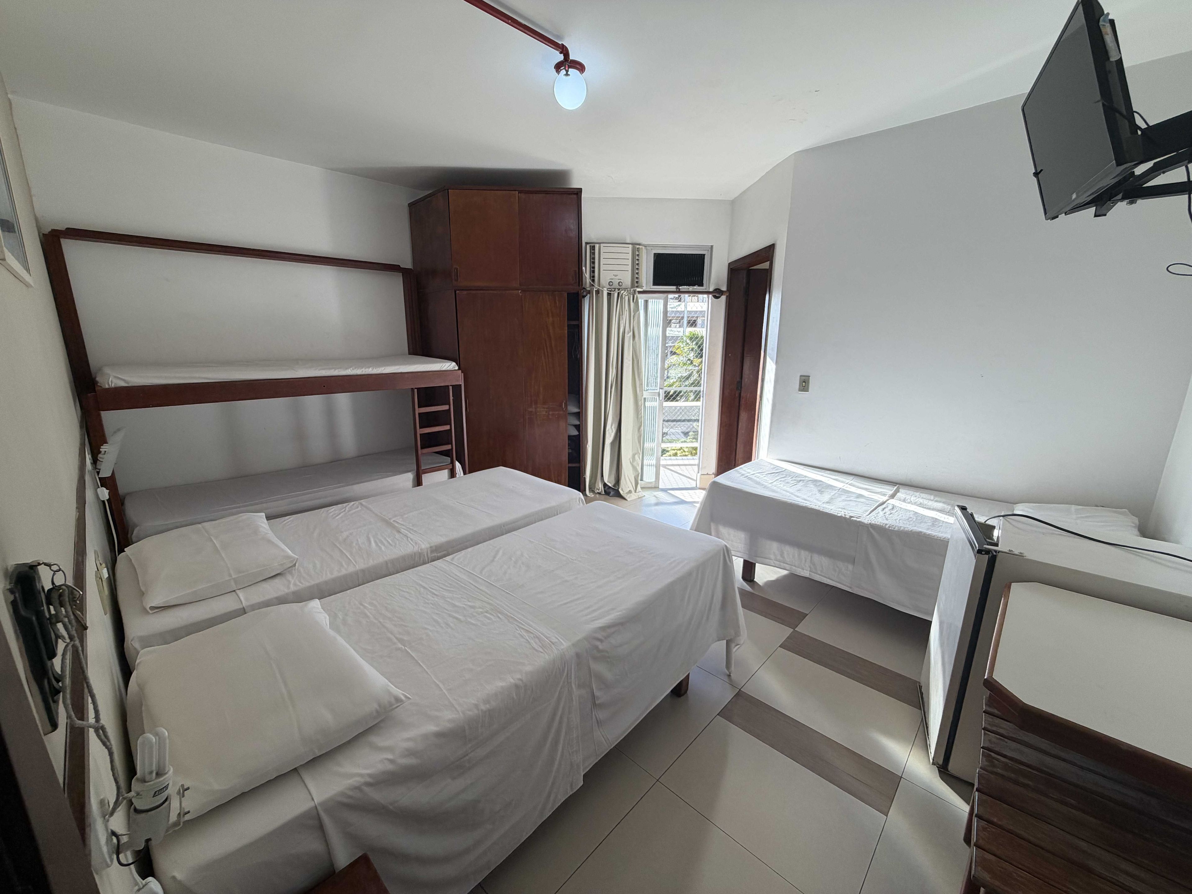 Un dormitorio con literas, un armario, un televisor y una ventana con cortinas.