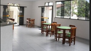A spacious room with large windows, wooden chairs with green cushions, and a tiled floor. - Joalpa Hotel Cabo Frio (Cabo Frio)