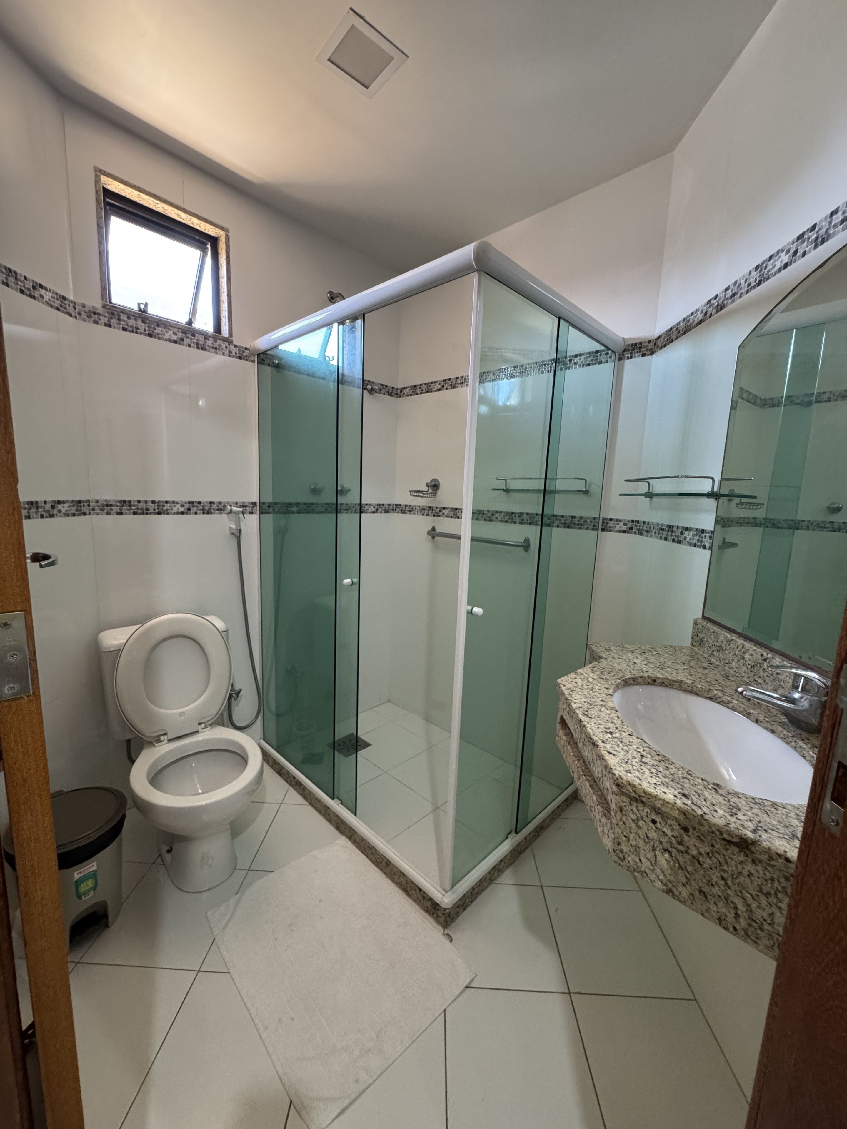 Ein Badezimmer mit einer gläsernen Duschkabine, einem Waschbecken mit Granitplatte und einer Toilette.
