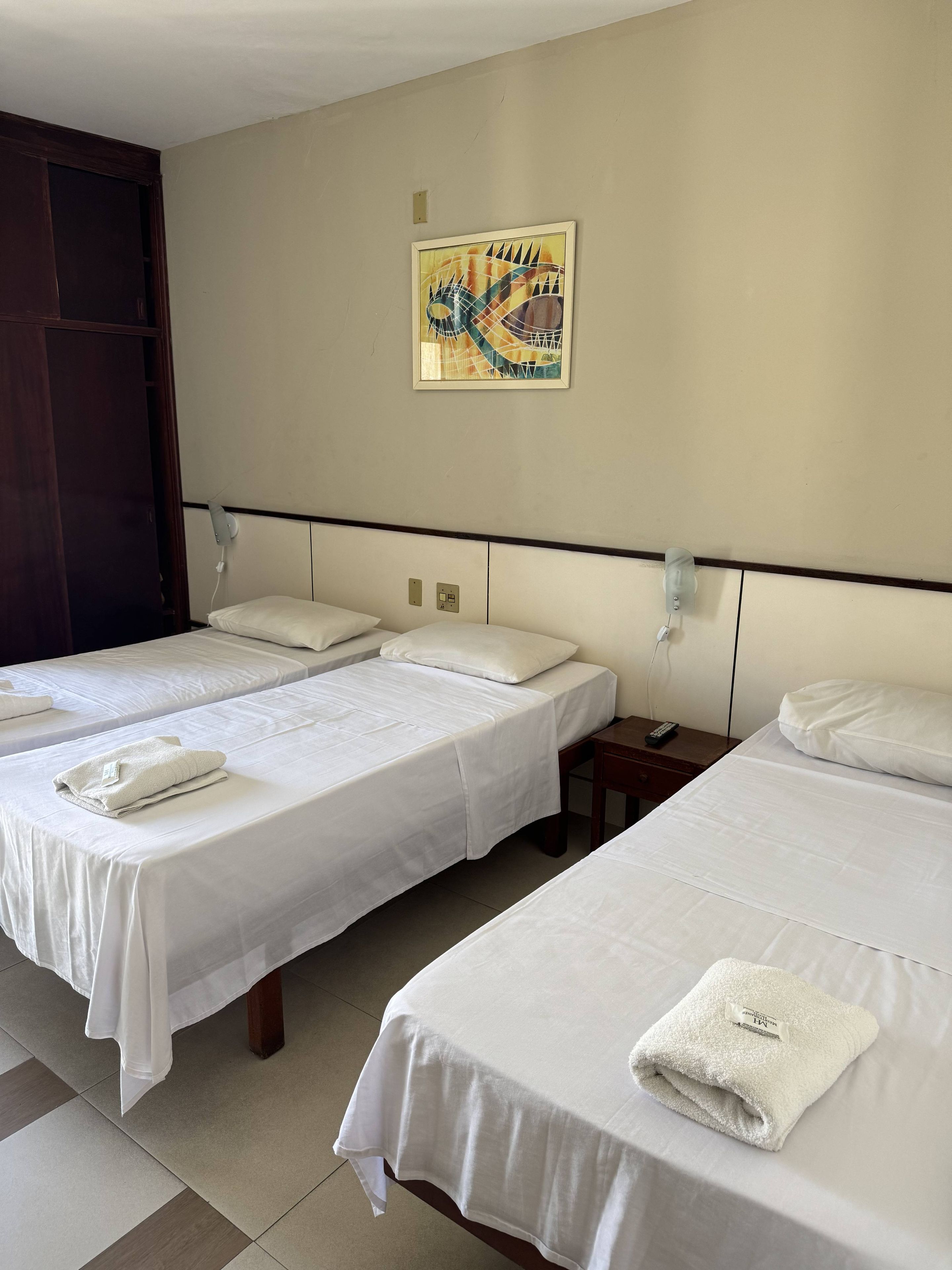 A hotel room with two beds, each with white linens and towels. There is a painting on the wall above the beds.