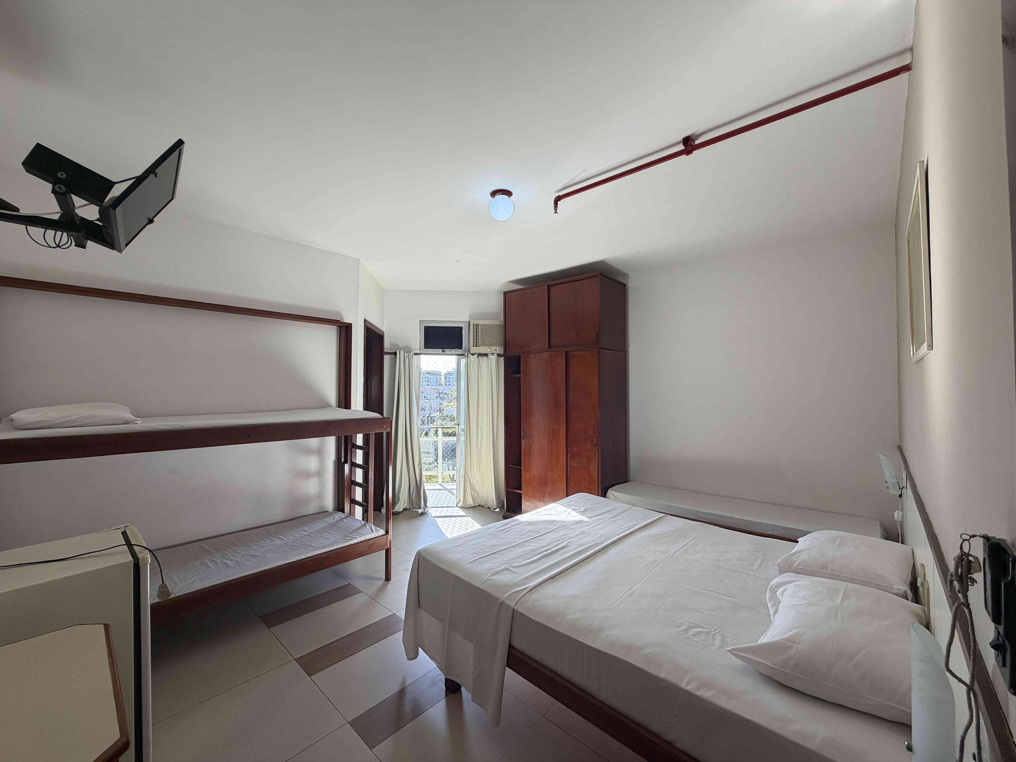 A bedroom with a bunk bed, a single bed, a wardrobe, and a window with curtains.