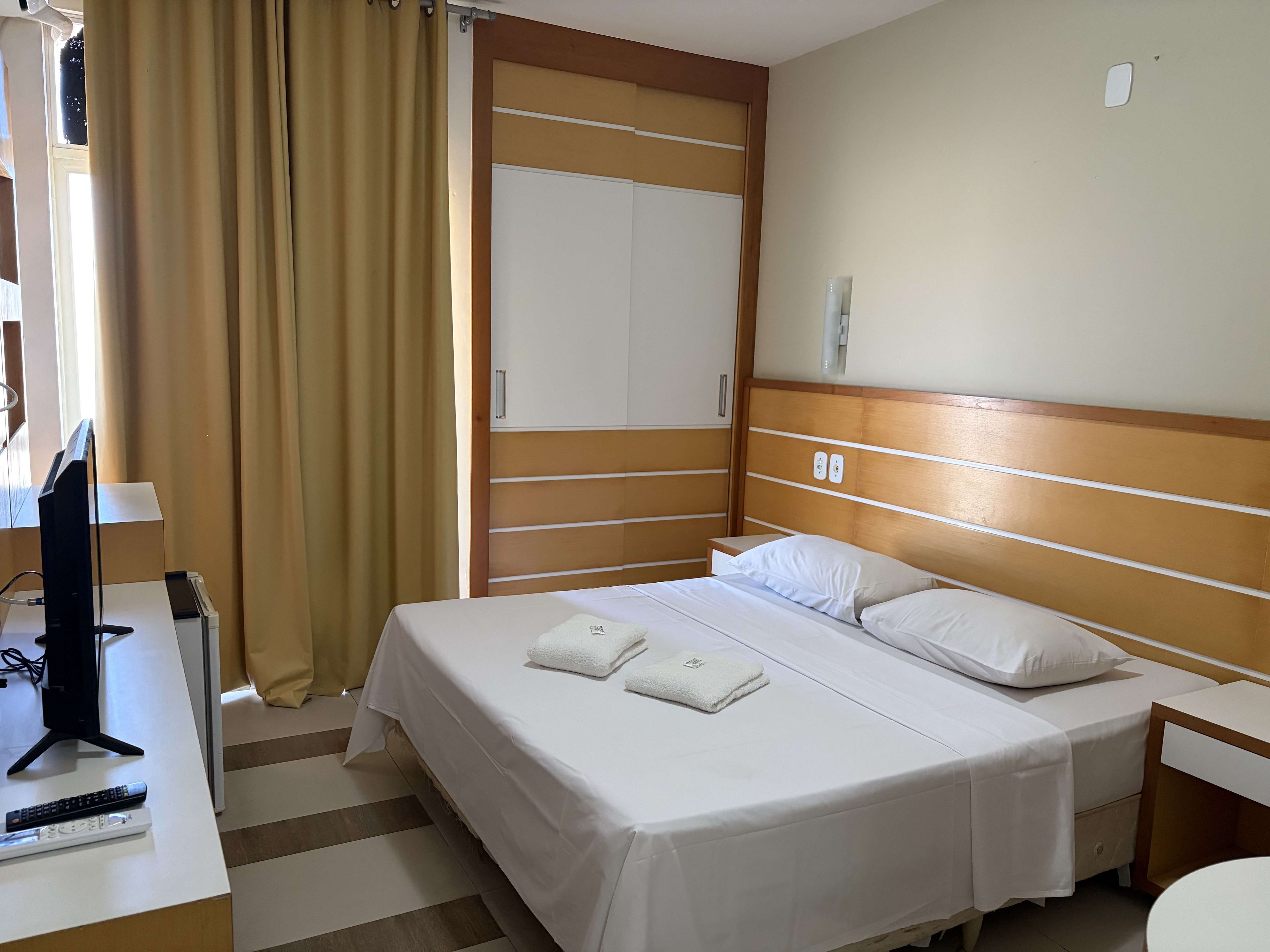 A hotel room with a bed, bedside table, and a desk with a computer and remote control.