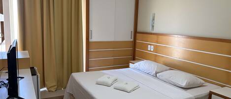 A hotel room with a bed, bedside table, and a desk with a computer and remote control.