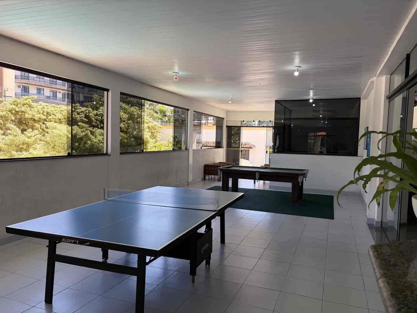Una habitación con mesa de ping pong, mesa de billar y amplios ventanales con vista a zonas verdes.