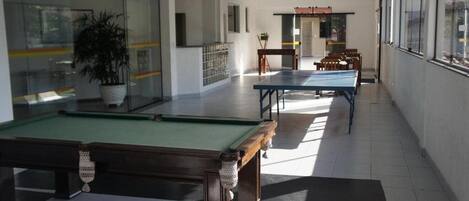 A pool table in a room with a glass wall, a potted plant, and a seating area with chairs.