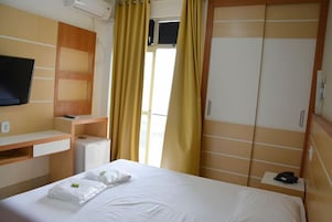 Habitación de hotel con cama, escritorio con computadora, televisor y armario.