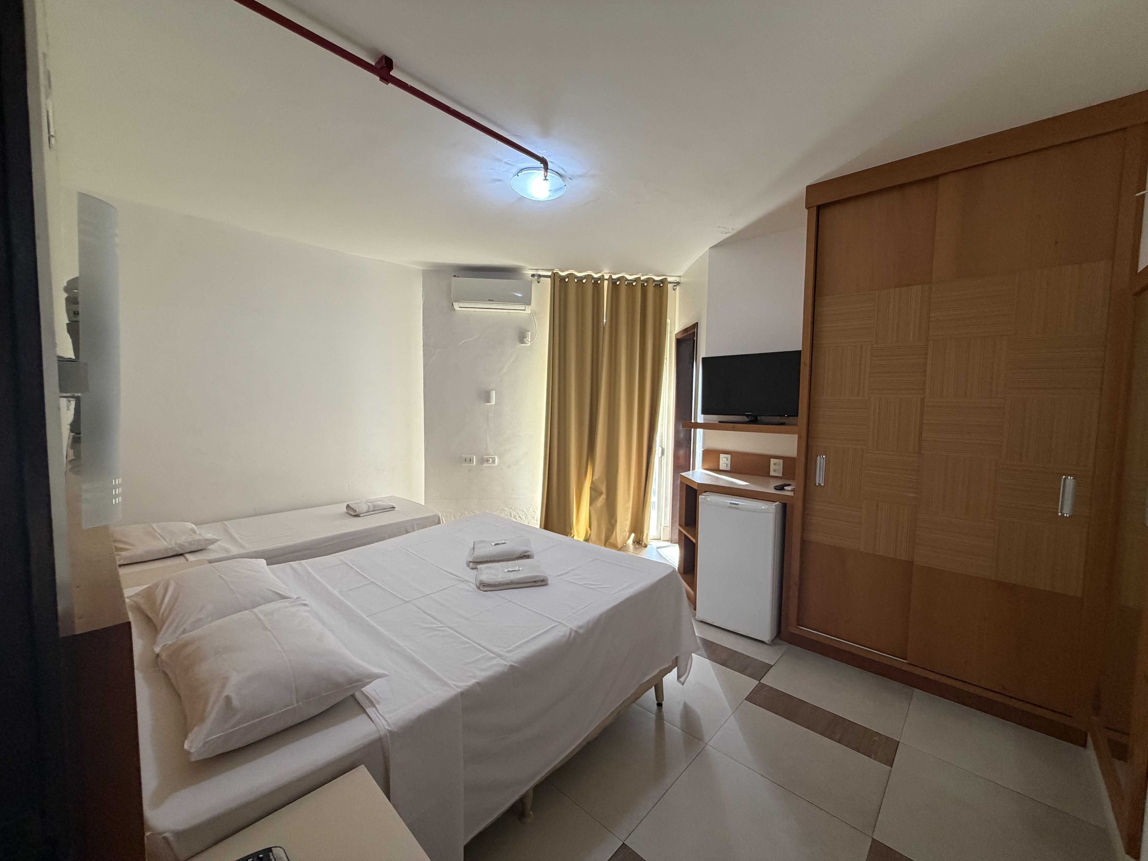 A hotel room with two beds, a television, a wardrobe, and a small refrigerator.