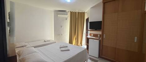 A hotel room with two beds, a television, a wardrobe, and a small refrigerator.