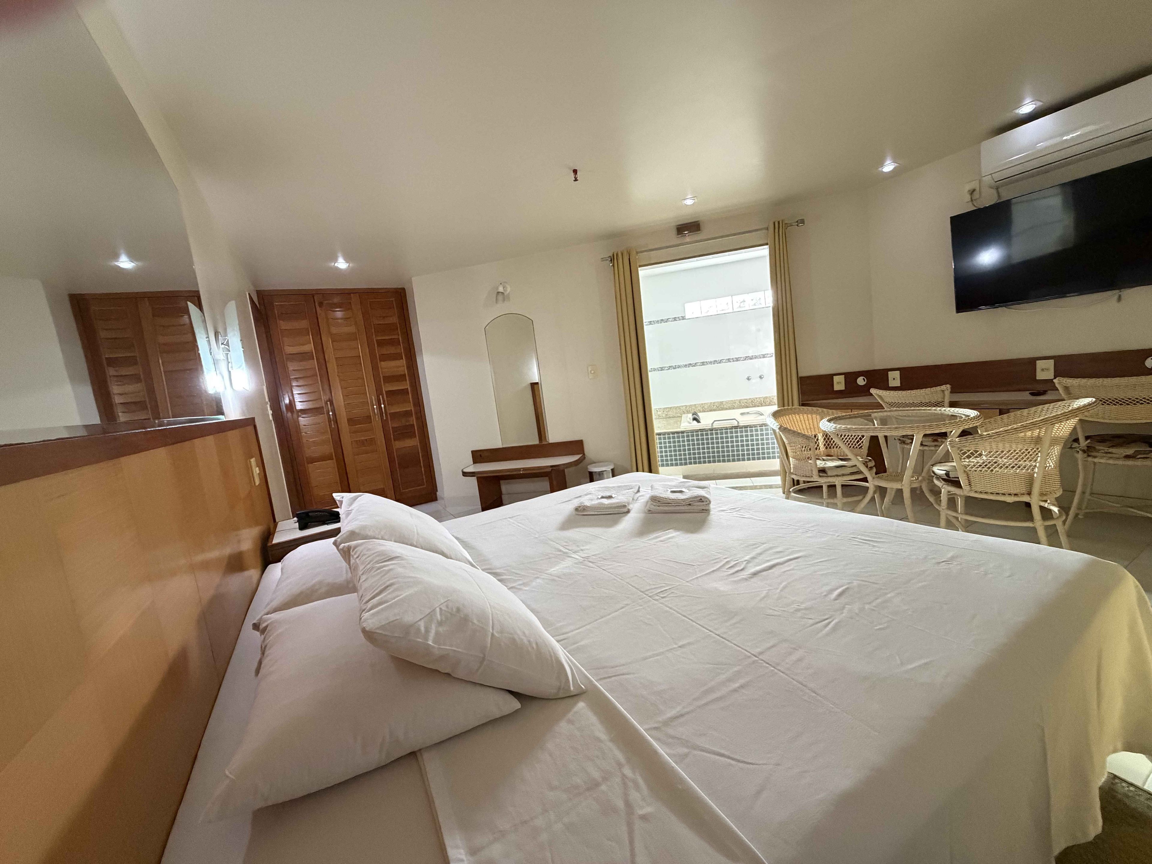 Una camera d'albergo con un letto, una scrivania, una sedia, una televisione e un balcone con vista.