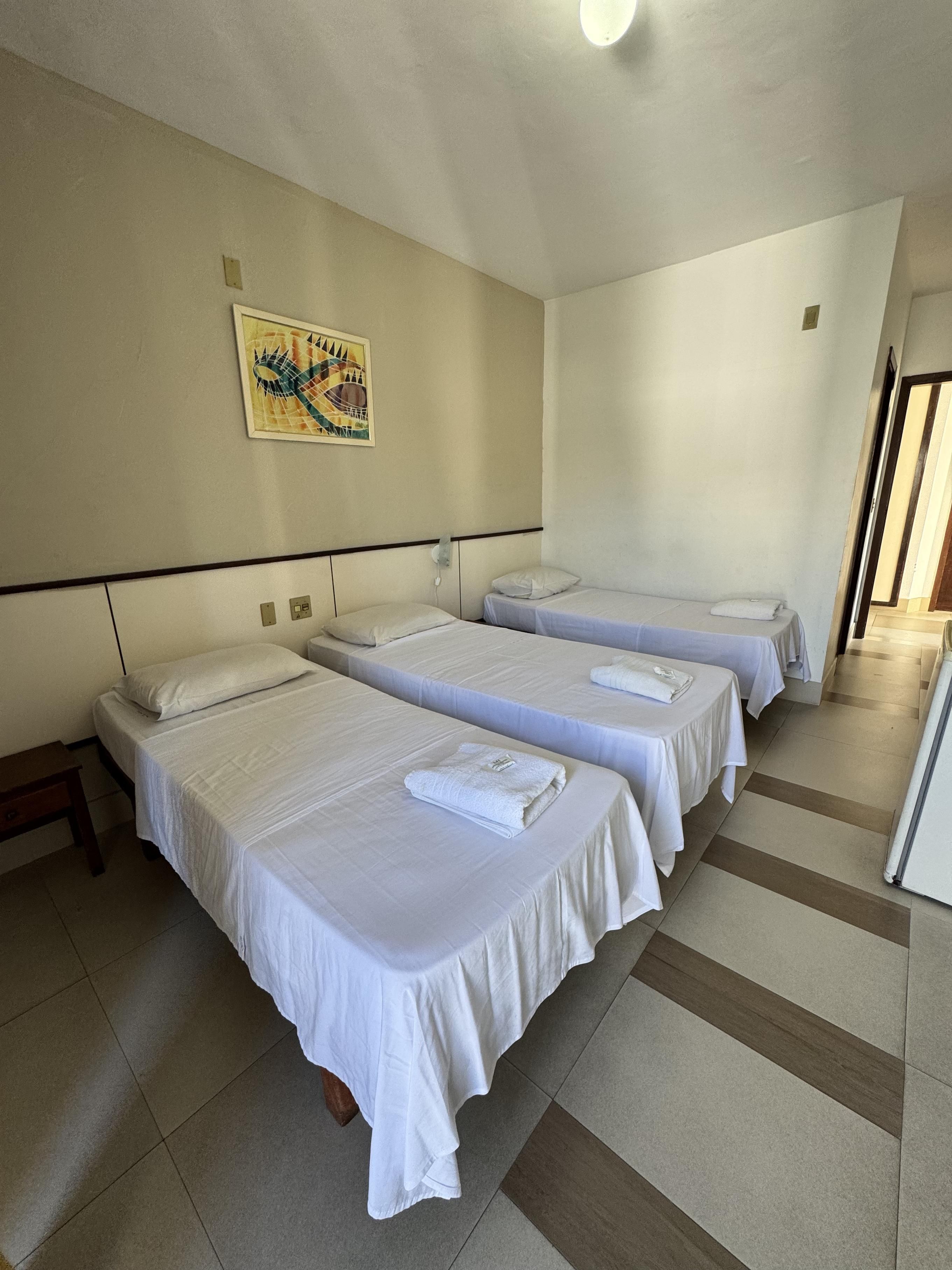 Una habitación de hotel con tres camas individuales, una mesita pequeña, una lámpara fijada a la pared y un cartel.