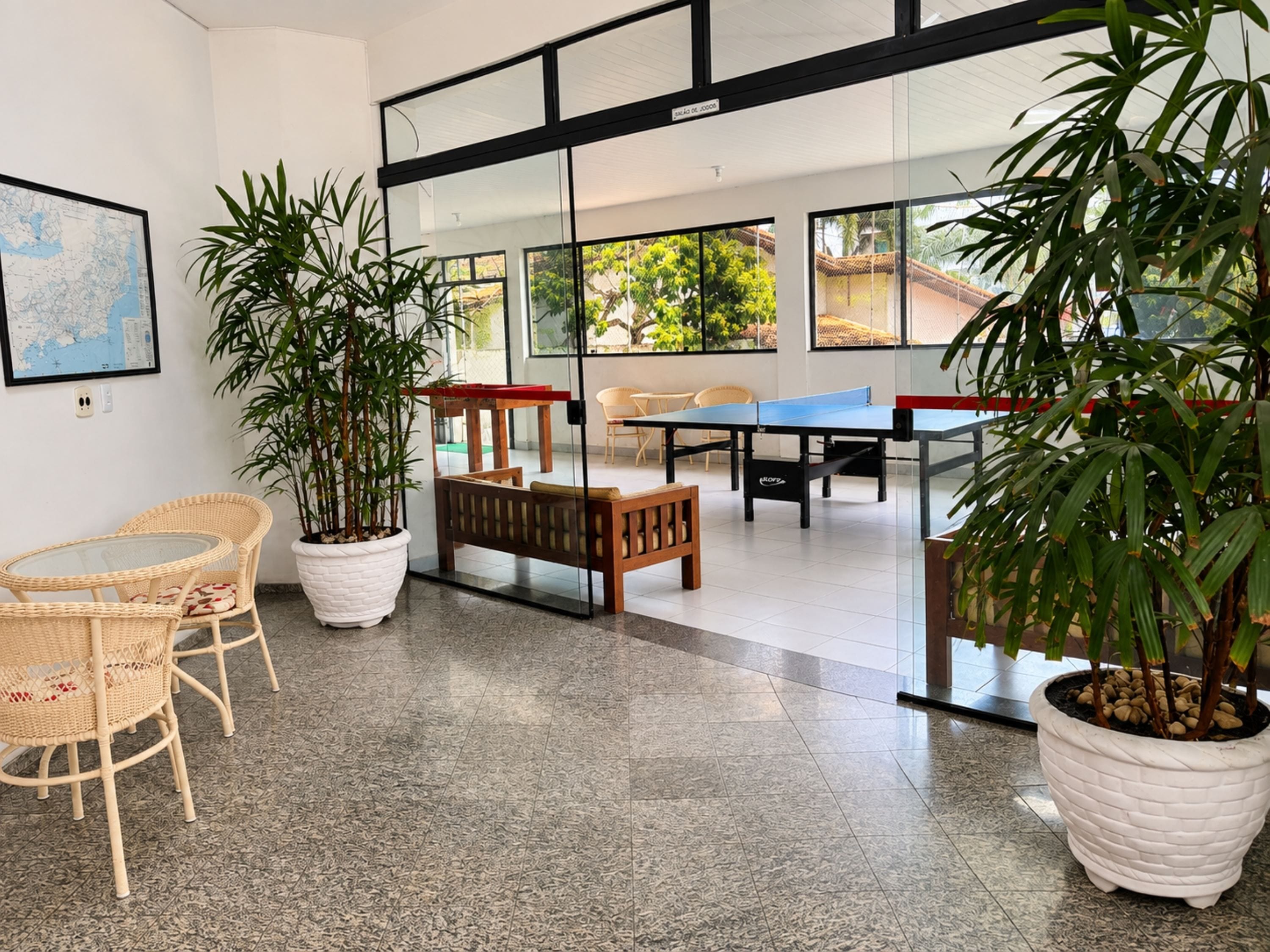 Una habitación con un separador de vidrio, un mapa en la pared, una mesa con sillas y dos plantas en macetas.