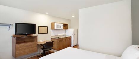 Habitación de hotel con cama, escritorio con silla, televisión, microondas, refrigerador y una pequeña kitchenette.