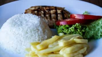 Een bord met witte rijst, gegrild vlees, frieten, sla en plakjes tomaat.