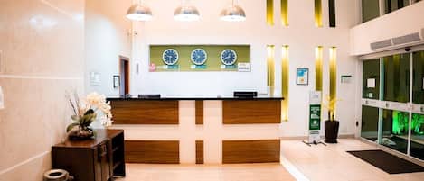 A reception area with a wooden reception desk, three clocks, and a potted plant.