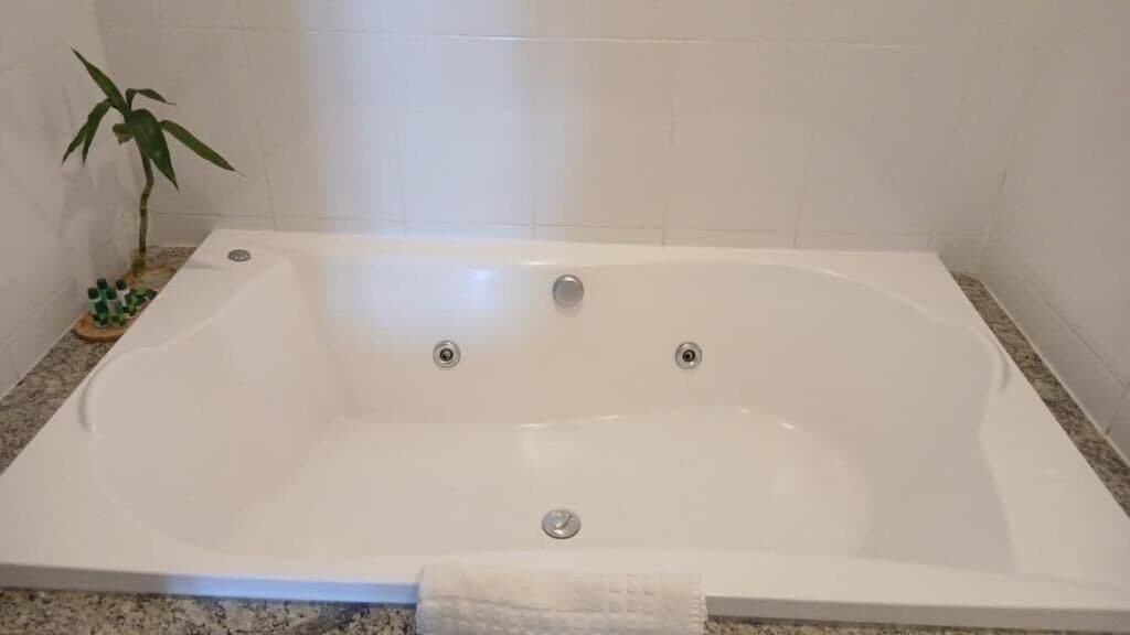 A rectangular bathtub with three faucets, a small plant, and a bottle of shampoo on a tray.