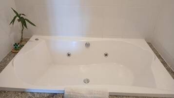 A rectangular bathtub with three faucets, a small plant, and a bottle of shampoo on a tray.
