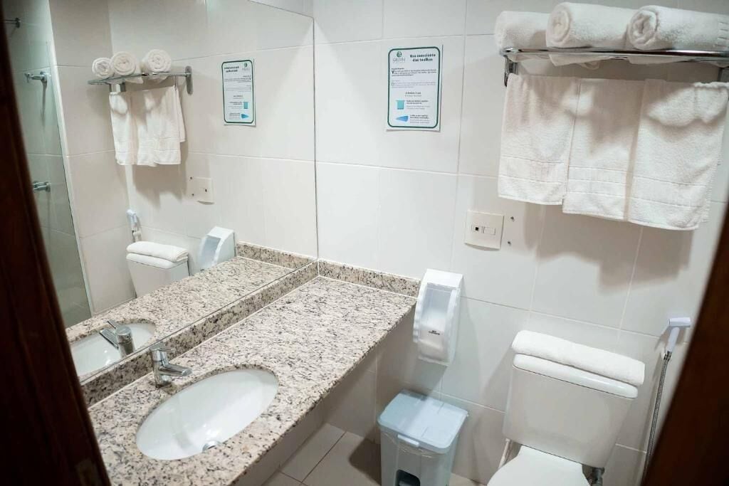 Un baño con lavamanos de granito, dos inodoros y un perchero con toallas dobladas.
