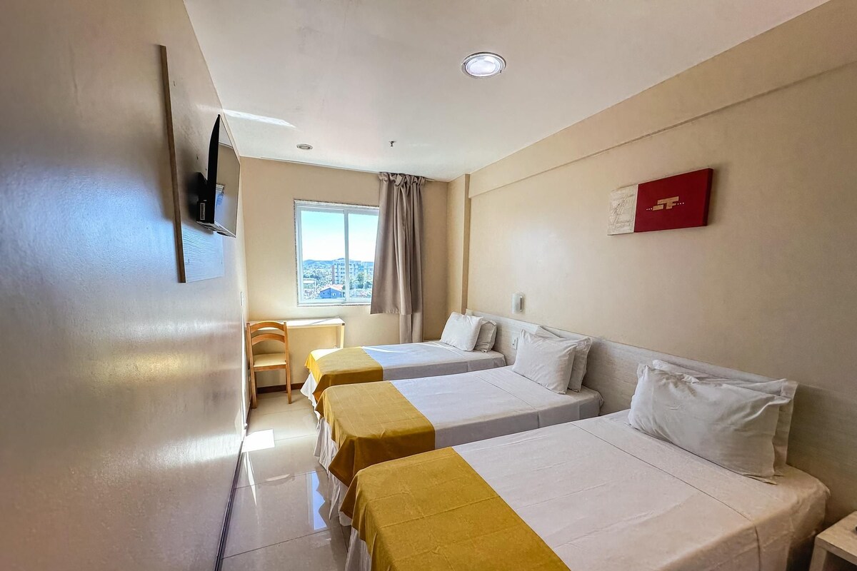 A hotel room with two beds, a TV mounted on the wall, a window with a view, and a desk with a chair.