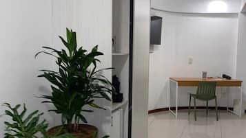 Une pièce moderne et minimaliste, dotée d’une porte coulissante, d’un bureau avec une chaise et de plusieurs plantes en pot.