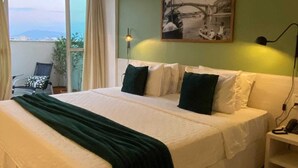 Une chambre avec un grand lit, un mur vert, un tableau représentant un pont et un balcon avec une chaise et une plante.