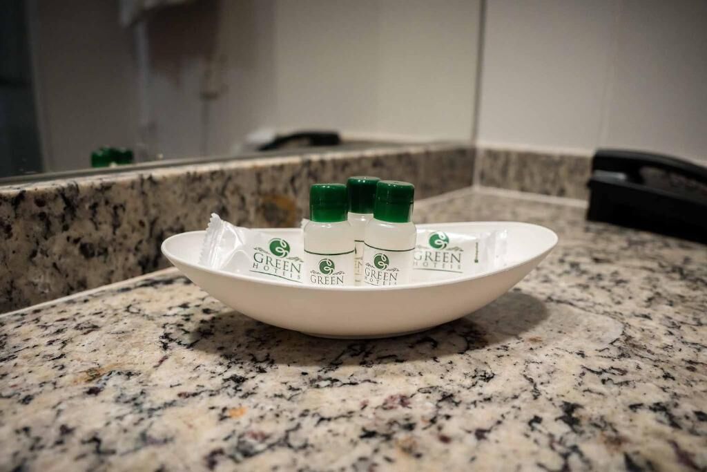 A white bowl on a granite countertop with three green bottles labeled "Green Hotel" and a white object in the bowl.