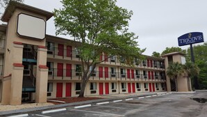 A multi-story motel with red doors and balconies, a parking lot, and a sign for Tricove Inn & Suites. - Tricove Inn & Suites (Jacksonville)