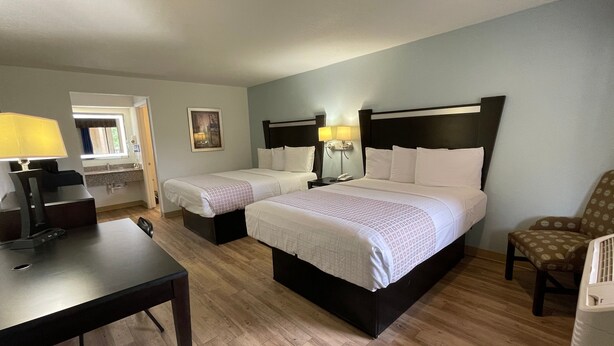 A hotel room with two single beds, a desk with a lamp, a chair, and a small table. - Tricove Inn & Suites (Jacksonville)