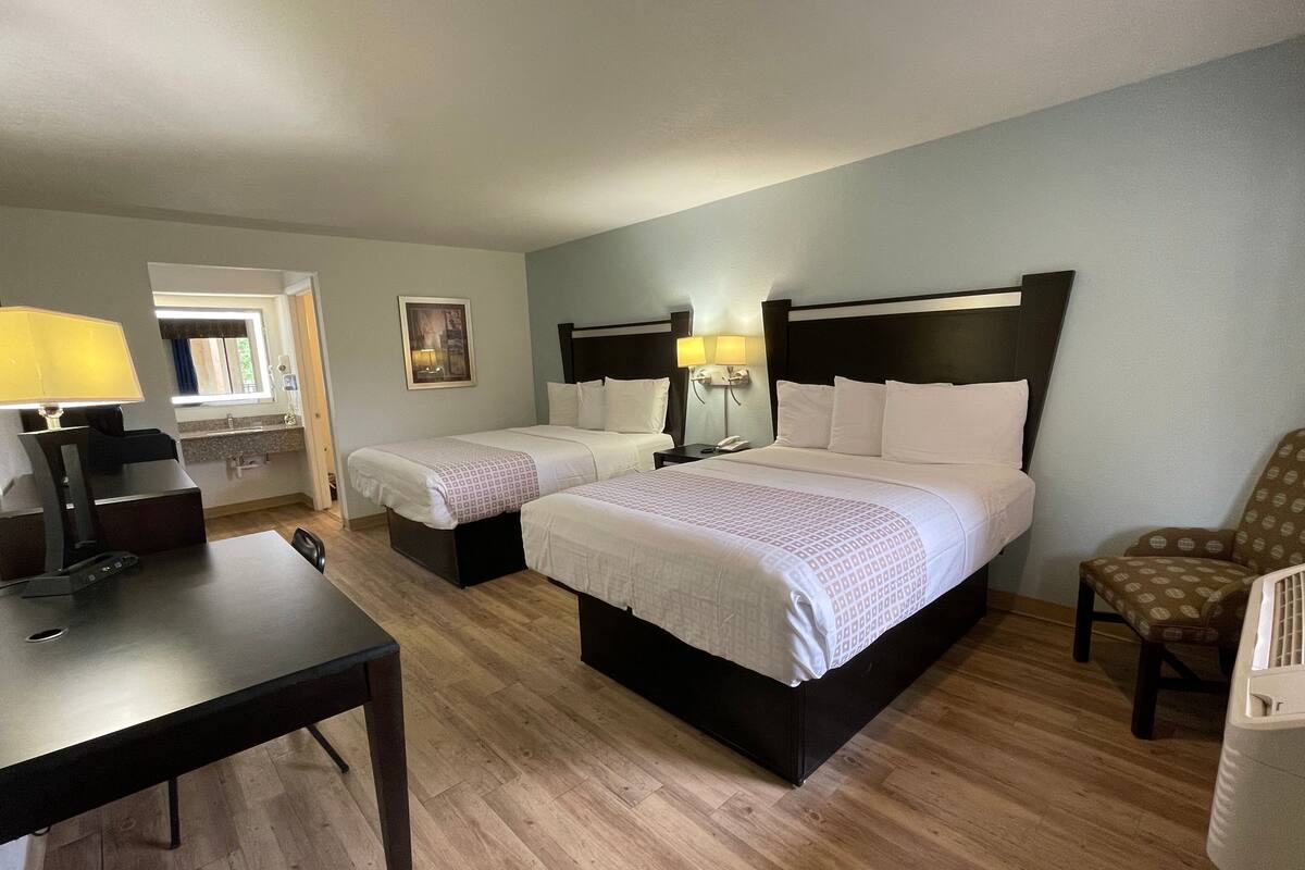 A hotel room with two single beds, a desk with a lamp, a chair, and a small table.