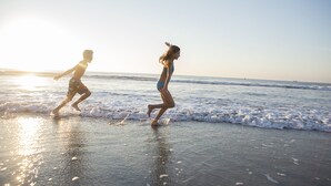Dos personas corriendo en una playa con el océano al fondo.