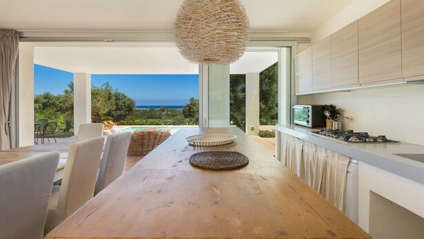 Una cocina moderna con una mesa de madera, lámpara de techo tejida y vista al océano.