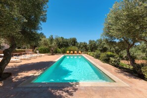 A rectangular swimming pool with clear blue water, surrounded by a paved deck. There are lounge chairs and a small table on the left side. - Villa Lisy (Carovigno)