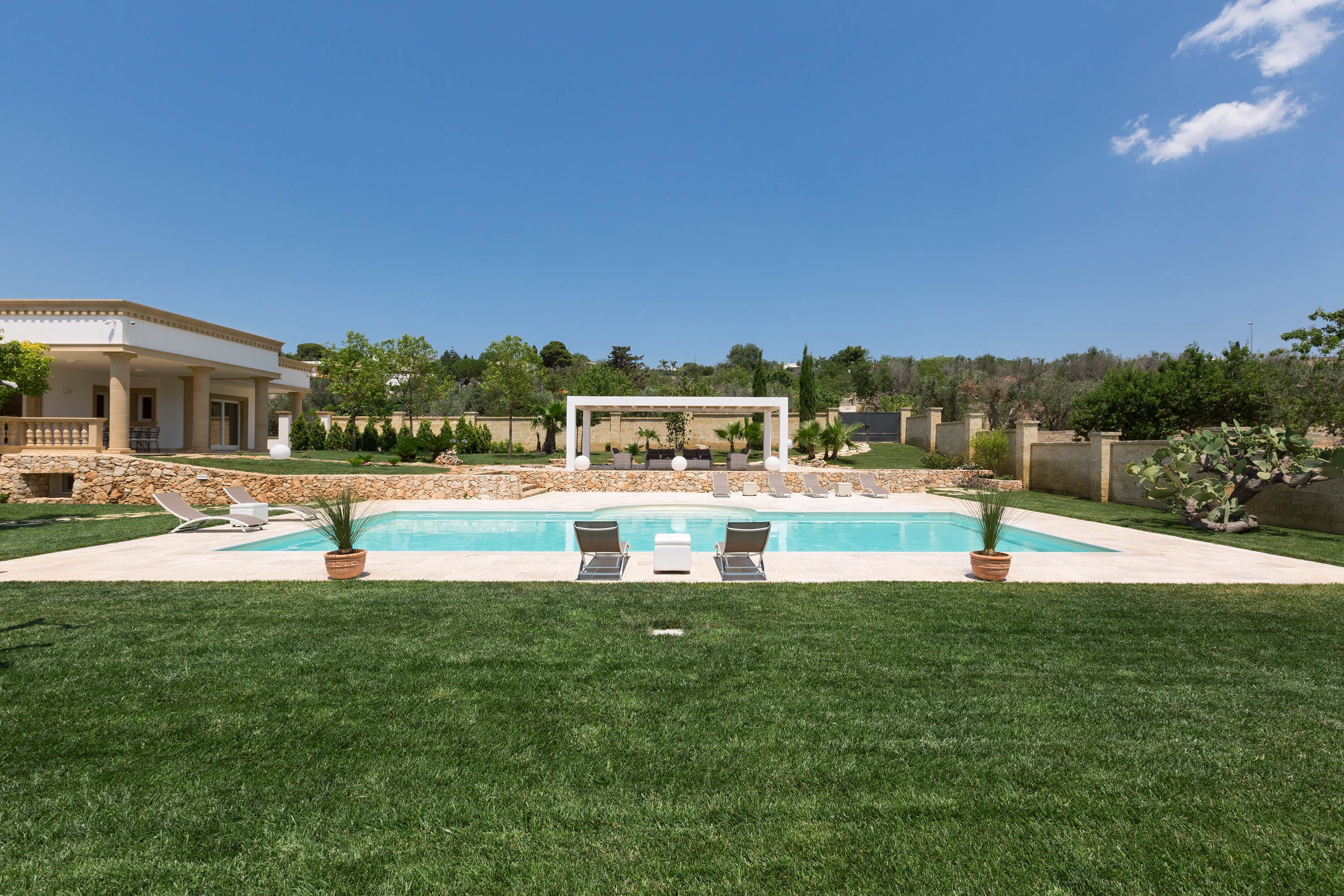Um quintal com piscina, cadeiras de sol e um pergolado.