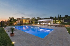 Una piscina con deck de piedra, un porche cubierto y una casa al fondo.