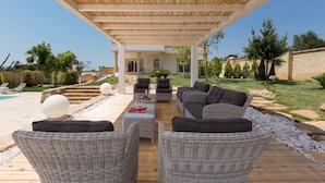 Un patio al aire libre con mobiliario de mimbre, una piscina y un muro de piedra.