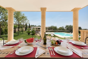 Mesa de comedor preparada para cuatro personas, con platos, cubiertos y vasos, con vistas a una piscina y jardín.