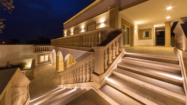 Una gran escalera con barandillas ornamentales que conduce a un balcón, rodeada de detalles arquitectónicos bien iluminados.