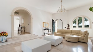 A spacious living room with a beige sectional sofa, a white coffee table, and a chandelier. - Villa Maria Clara (Gagliano del Capo)