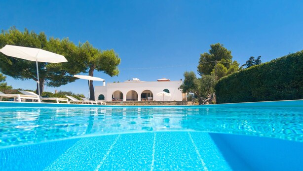 A clear blue pool with a view of a white building with arches in the background. - Villa Maria Clara (Gagliano del Capo)