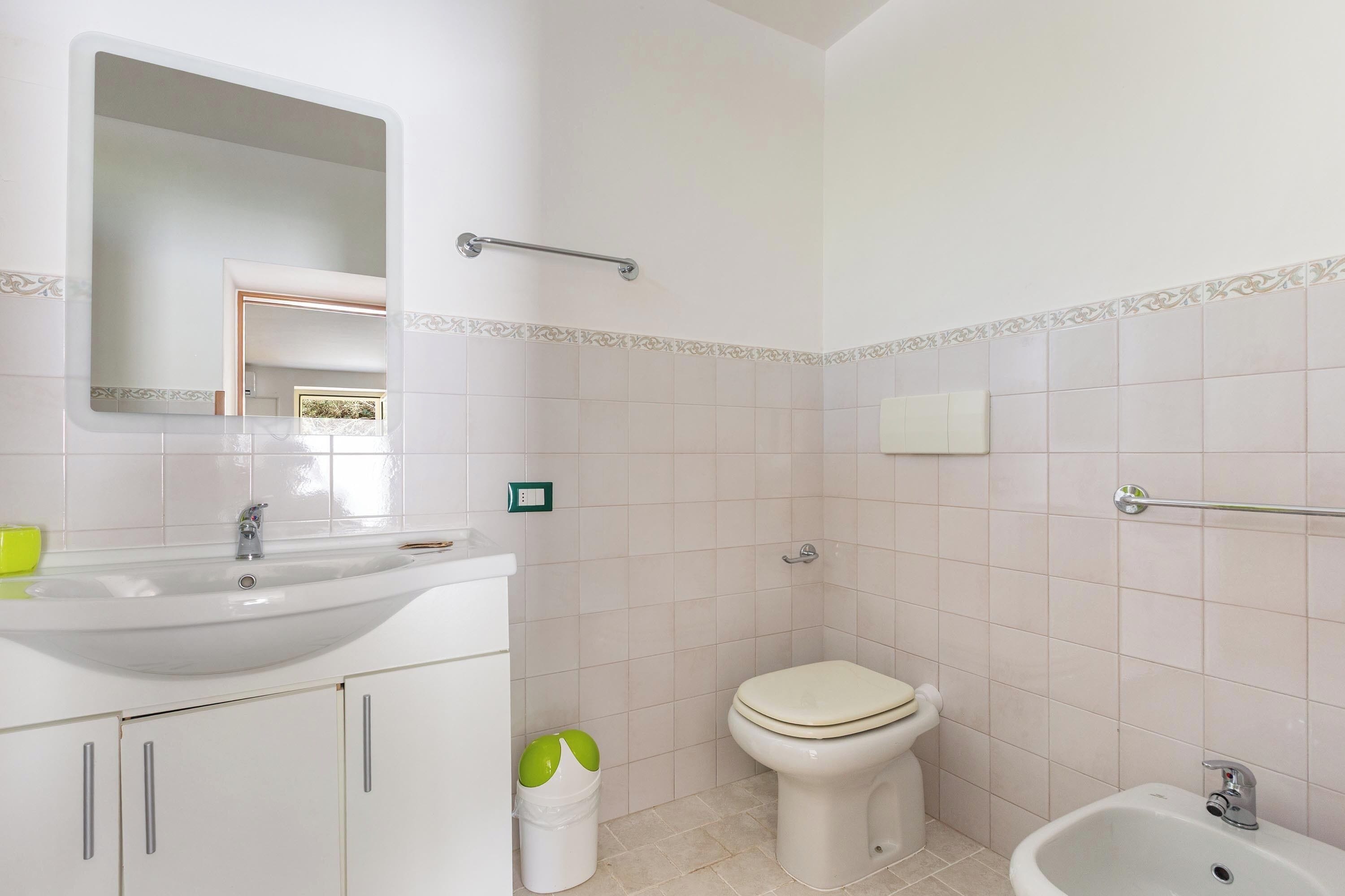 Un bagno con lavandino, WC e bidet, dotato di specchio, porta asciugamani e cestino.