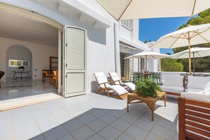 A spacious outdoor patio with tiled flooring, white lounge chairs, and large umbrellas providing shade.