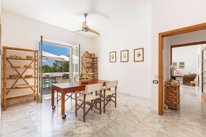 A dining area with a wooden table and chairs, a ceiling fan, and a view through an open door to an outdoor patio.